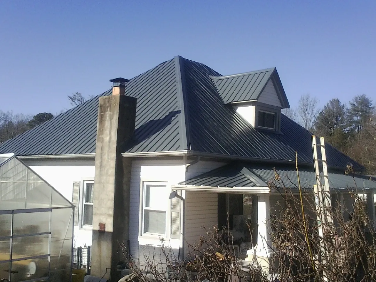 Dark blue standing seam metal roof on a white farmhouse with dormer — Slate & Tile Roof Repair by Roofing Brothers in Kellerton