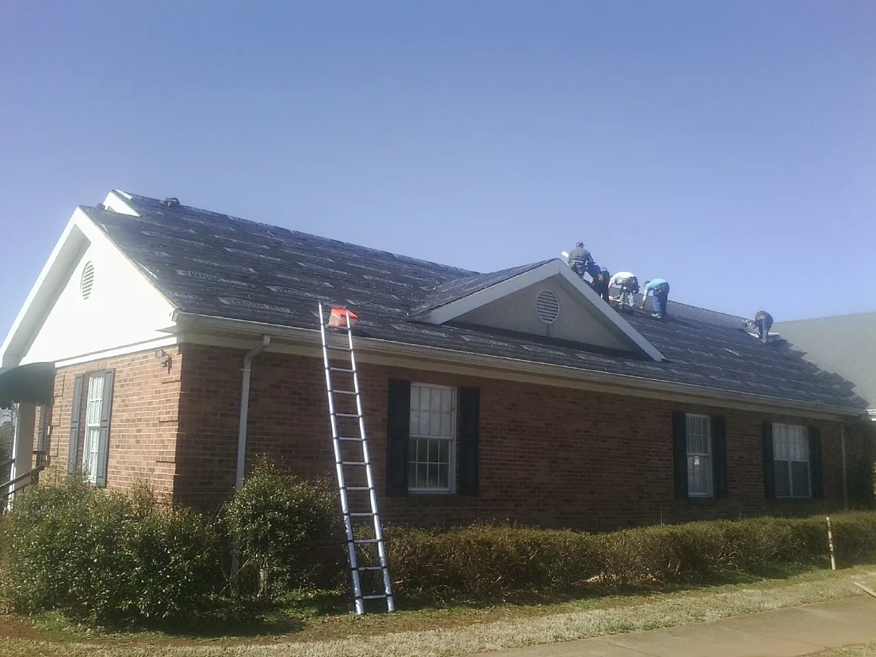 Crew tearing shingles off a brick ranch roof with a ladder set — Emergency Roof Repair work by our crew in Kellerton