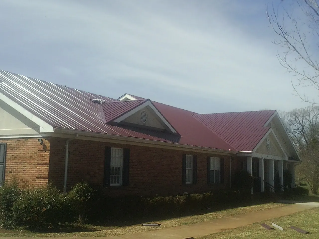 Red metal roof with gabled entries on a long brick building, from a Hail Damage Roof Repair job in Kellerton