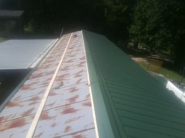 Old rusted panels beside newly installed green metal roofing — Wind Damage Roof Repair by Roofing Brothers in Kellerton