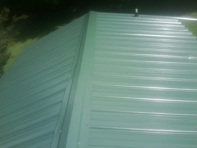 New green metal panels meeting at the ridge of a roof — Flat Roof Repair work by our crew in Kellerton