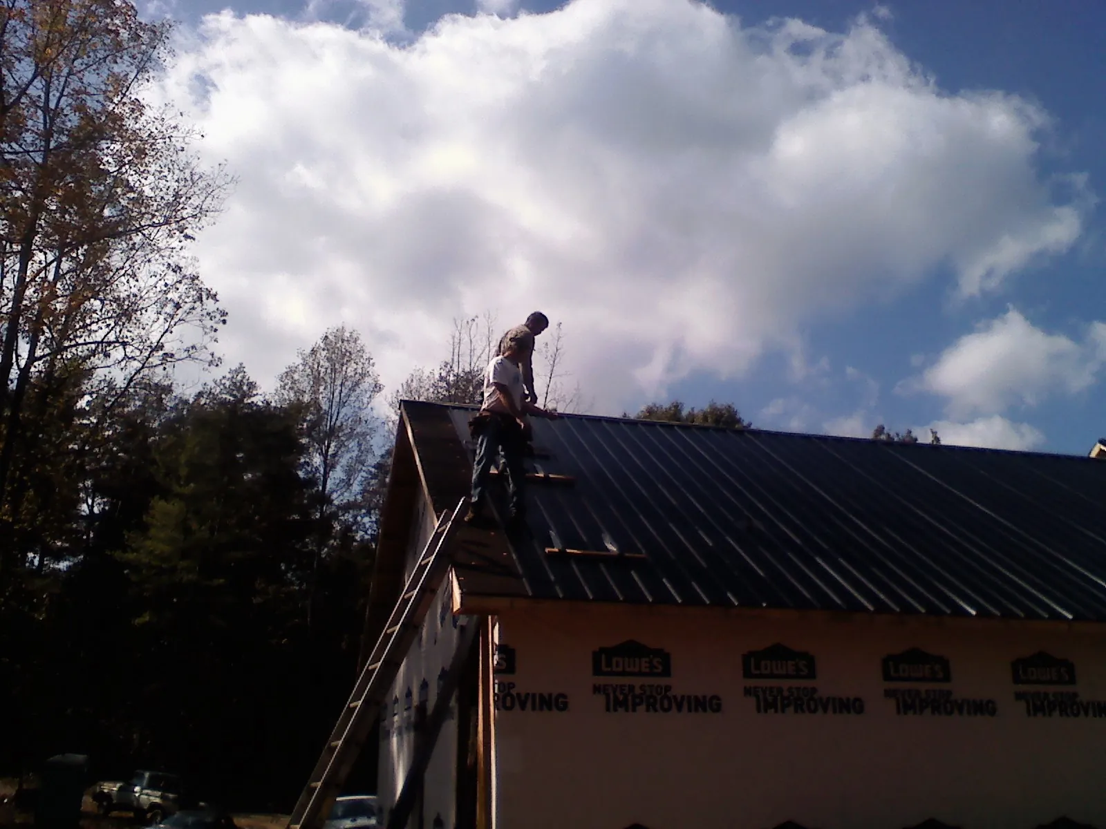 Roofer fastening dark metal panels high against a cloudy sky, from a Roof Inspection job in Kellerton