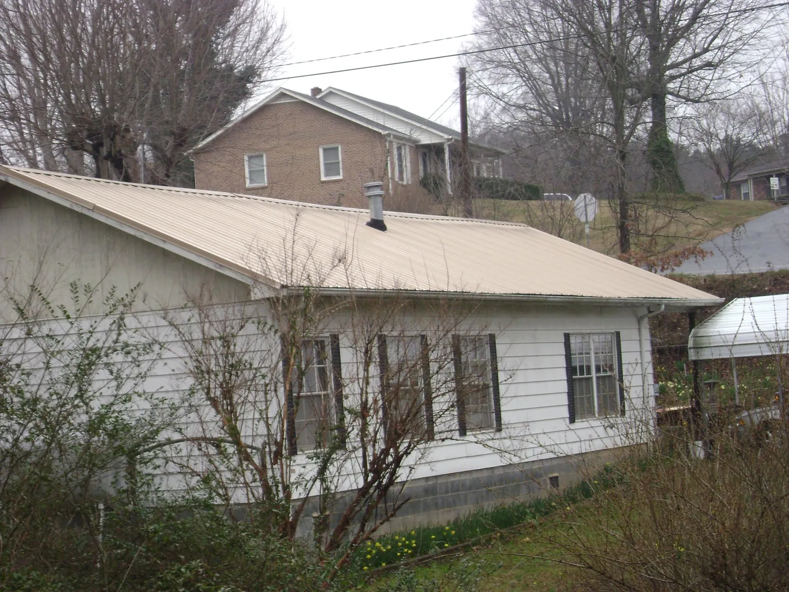 Tan metal roof on a white sided house set into a hillside — Commercial Roofing by Roofing Brothers in Kellerton