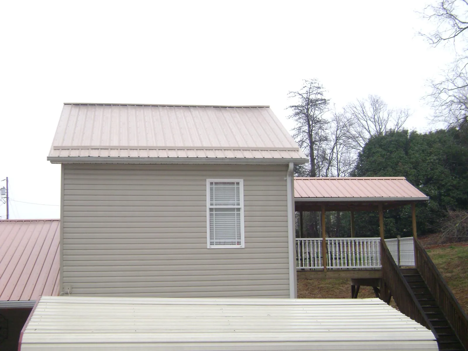 Tan metal roofs on a two story addition and attached porch, from a Roof Replacement job in Kellerton
